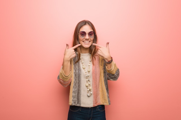 La mujer joven del hippie en fondo rosado sonríe, señalando la boca