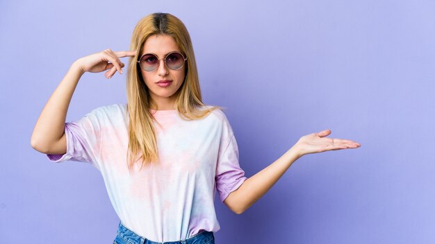 Mujer joven hippie con gafas sosteniendo y mostrando un producto en la mano.