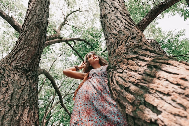 Mujer joven hippie de pie cerca de un árbol viejo