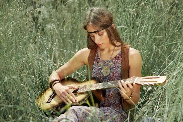 Mujer joven hippie tocando la guitarra sentada en el césped