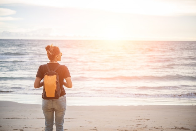 Mujer joven hipster con mochila de pie por la playa.