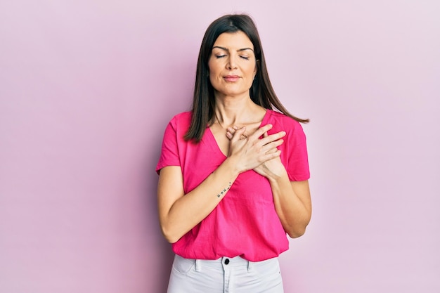 Mujer joven hispana con ropa casual sonriendo con las manos en el pecho con los ojos cerrados y un gesto de agradecimiento en el concepto de salud facial