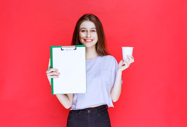 mujer joven con hoja de informe y una taza de bebida.