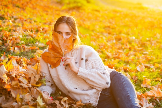 Mujer joven con hojas de otoño en la mano y arce amarillo de otoño. Presentación soñadora de la muchacha coqueta.