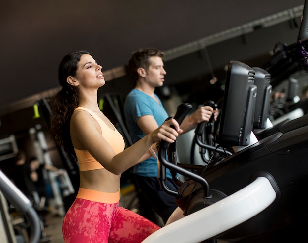 Mujer joven y hombre en el entrenador paso a paso elíptico que ejercita en gimnasio