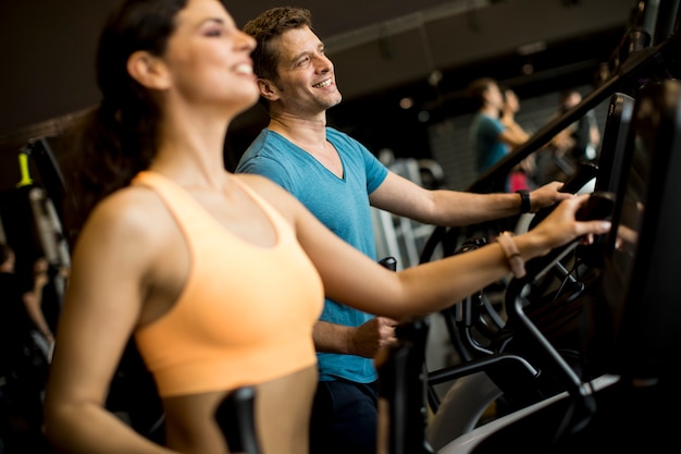 Mujer joven y hombre en el entrenador paso a paso elíptico que ejercita en gimnasio