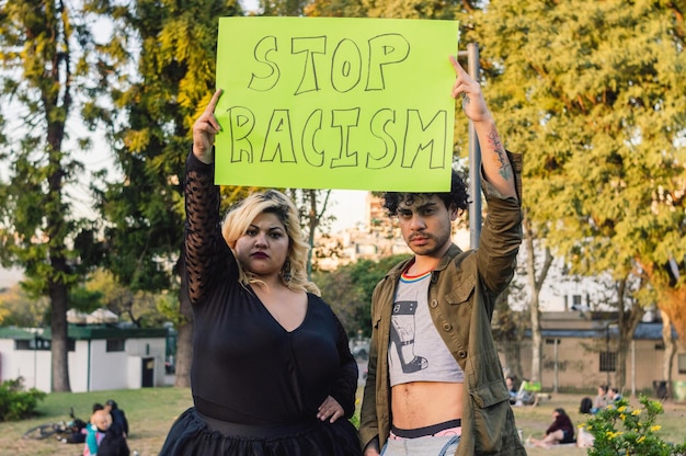 Mujer joven y hombre homosexual al aire libre protestando con un cartel que dice detener el racismo