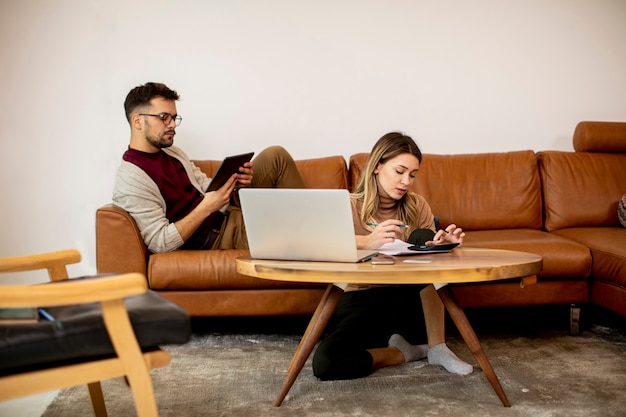 Mujer joven y hombre joven que usa la computadora portátil mientras está sentado en el sofá en casa