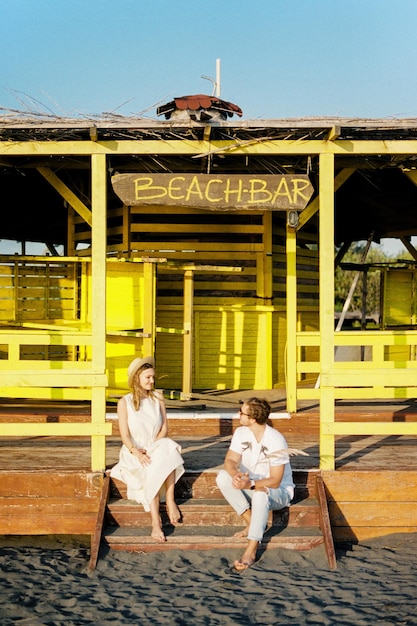 Mujer joven y hombre sentados en los escalones de madera de un bar en la playa