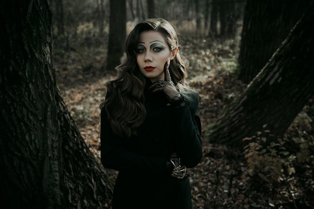 Una mujer joven en una imagen sombría gótica de una bruja en un traje de Halloween del bosque