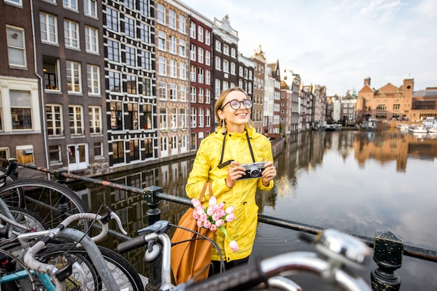 Mujer joven en impermeable amarillo con cámara de fotos disfrutando de la vista de la mañana en la hermosa vista del paisaje urbano en Amsterdam