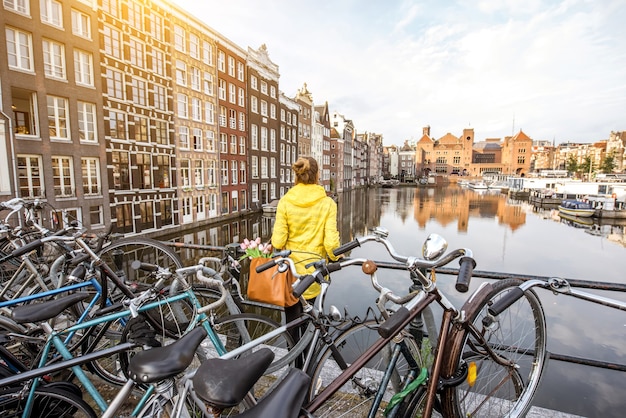 Mujer joven en impermeable amarillo disfrutando de la vista de la mañana en la hermosa vista del paisaje urbano en Amsterdam