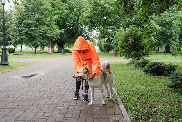 Mujer joven en impermeable naranja caminando con su perro en un parque