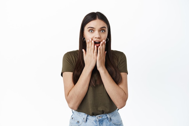 Mujer joven impresionada y sorprendida jadeando emocionada de escuchar noticias increíbles obteniendo un premio o ganando mirando con incredulidad y asombro de pie contra el fondo blanco