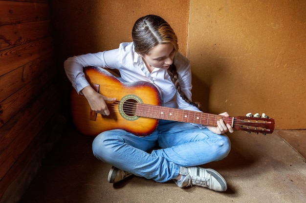 Mujer joven inconformista sentada en el suelo y tocando la guitarra en casa Chica adolescente aprendiendo a tocar canciones y escribiendo música en su habitación Estilo de vida de hobby relajarse Instrumento concepto de educación de ocio