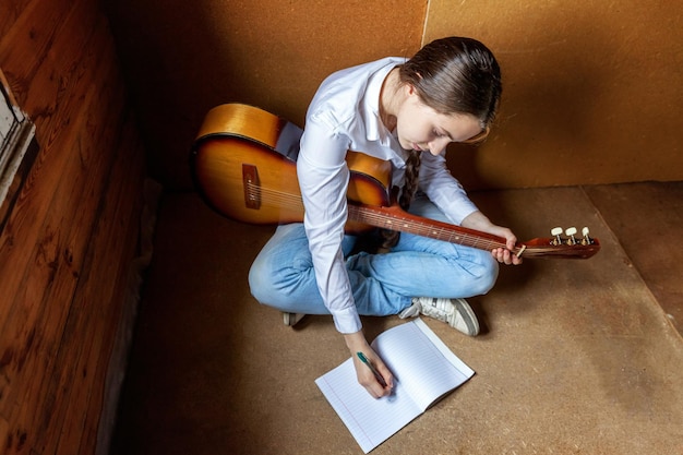 Mujer joven inconformista sentada en el suelo y tocando la guitarra en casa Chica adolescente aprendiendo a tocar canciones y escribiendo música en su habitación Estilo de vida de hobby relajarse Instrumento concepto de educación de ocio