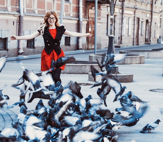 Mujer joven inconformista con vestido rojo en la ciudad. Palomas de primavera y pájaros.