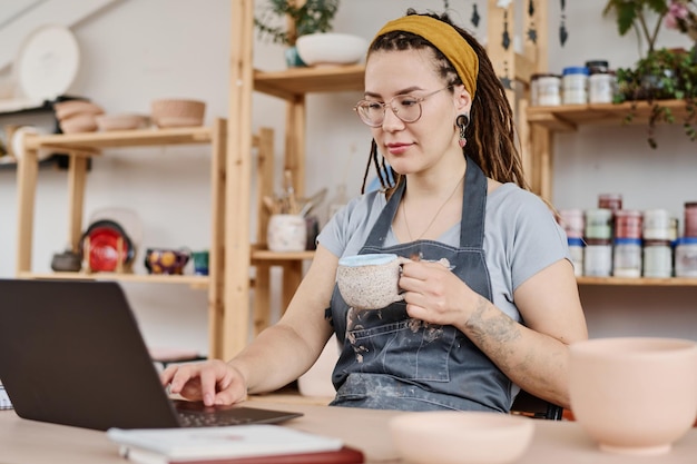 Foto mujer joven independiente o propietaria de una pequeña empresa sentada frente a una computadora portátil