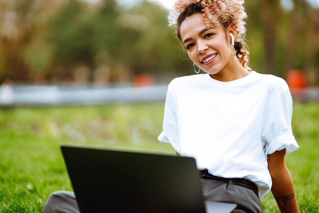 Mujer joven independiente que disfruta viendo un seminario web educativo en una computadora portátil sentada en la hierba verde