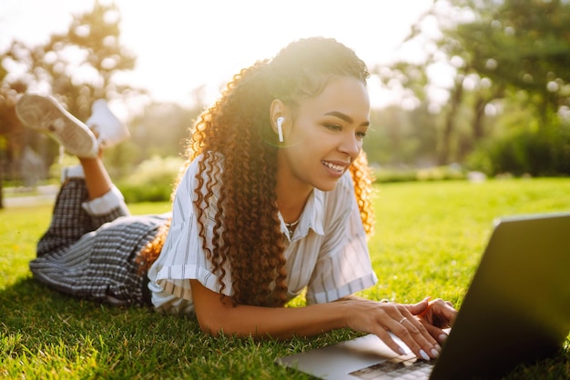 Mujer joven independiente sentada en la hierba verde con una computadora portátil Educación en línea