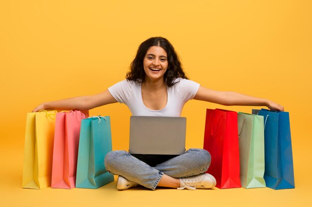 Mujer joven india adicta a las compras usando un portátil de fondo amarillo