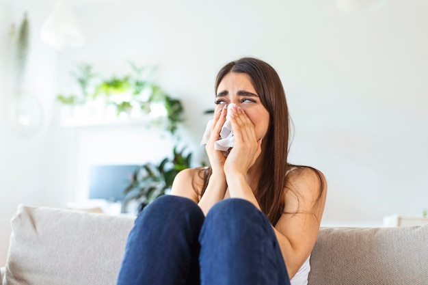 Mujer joven infeliz cubriendo la cara con las manos llorando sola cerca de la niña deprimida sentada en el sofá en casa problema de salud o pensando en malas relaciones romper con el novio divorcio