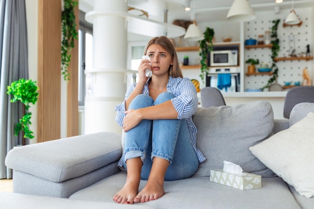 Mujer joven infeliz que cubre la cara con las manos llorando sola cerca de una chica deprimida sentada en el sofá en casa con problemas de salud o pensando en malas relaciones rompiendo con el divorcio de su novio