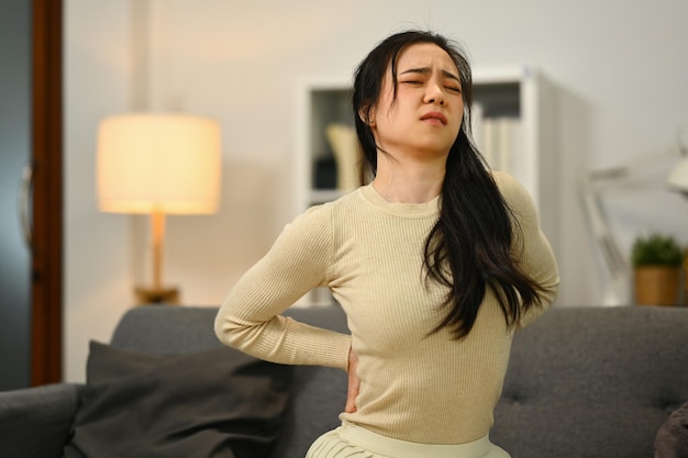 Mujer joven infeliz que sufre de dolor de espalda lumbar inferior Problemas de salud de la columna y concepto de atención médica