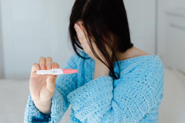 Mujer joven infeliz sosteniendo una prueba de embarazo que muestra un resultado negativo