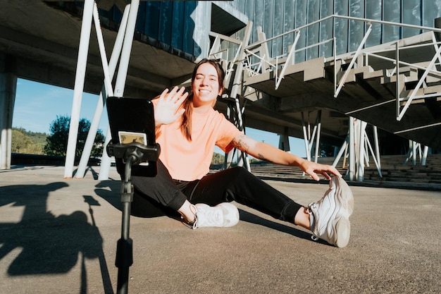 Mujer joven influyente en el fitness haciendo ejercicio y saludando mientras transmite con un teléfono inteligente a sus seguidores Deporte y estilo de vida saludable en el contenido de las redes sociales Conéctese con la audiencia