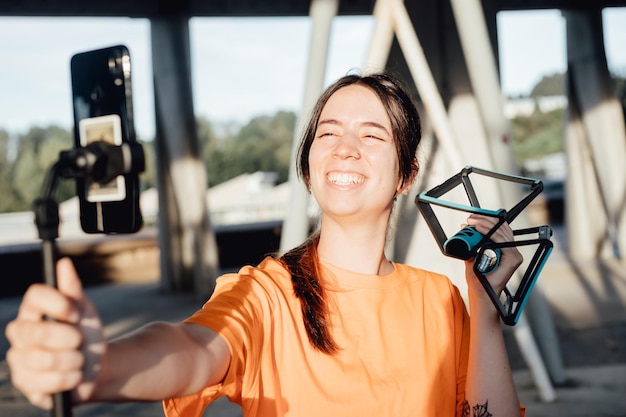 Mujer joven influyente en el fitness que muestra herramientas de flexión con un teléfono inteligente en un trípode a sus seguidores mientras transmite una rutina deportiva en línea Deporte y estilo de vida saludable en el contenido de las redes sociales