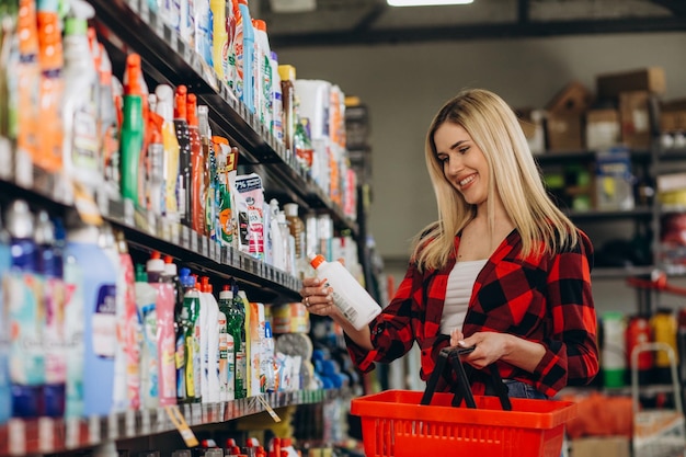 Mujer joven interesada haciendo compras en la tienda de productos químicos domésticos leyendo etiquetas en botellas