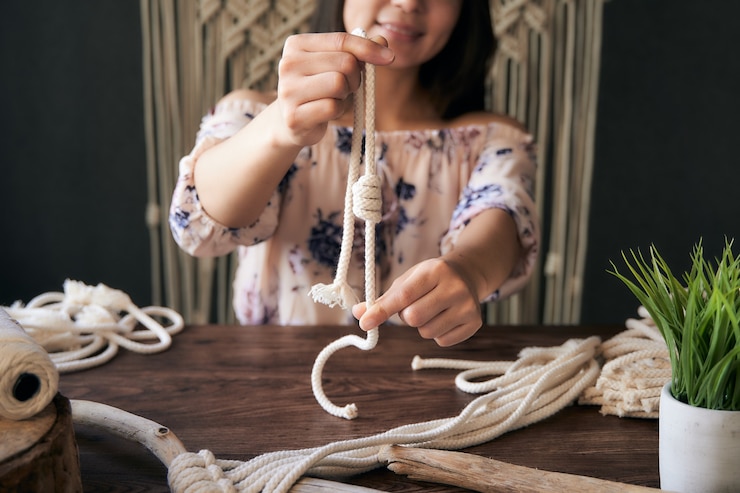 Foto mujer joven irreconocible y feliz mostrando un nudo de macramé en un espacio de trabajo
