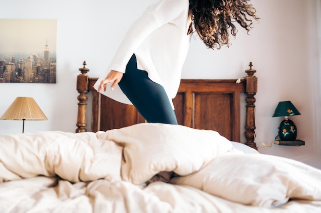 Foto mujer joven irreconocible saltando sobre la cama en el dormitorio