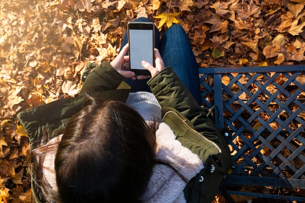 Mujer joven irreconocible usando teléfono inteligente en otoño