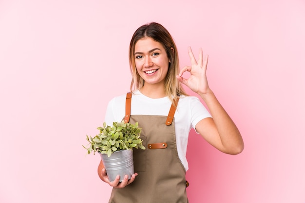 Mujer joven jardinero caucásico en un fondo rosa alegre y confiado mostrando gesto ok.