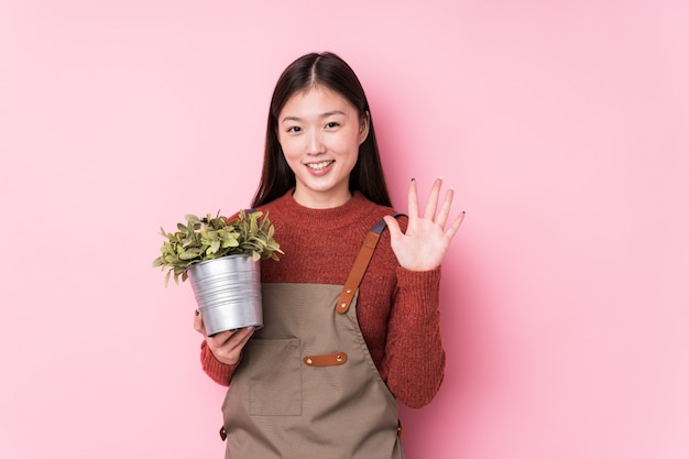 Mujer joven jardinero chino sosteniendo una planta sonriente alegre mostrando el número cinco con los dedos.