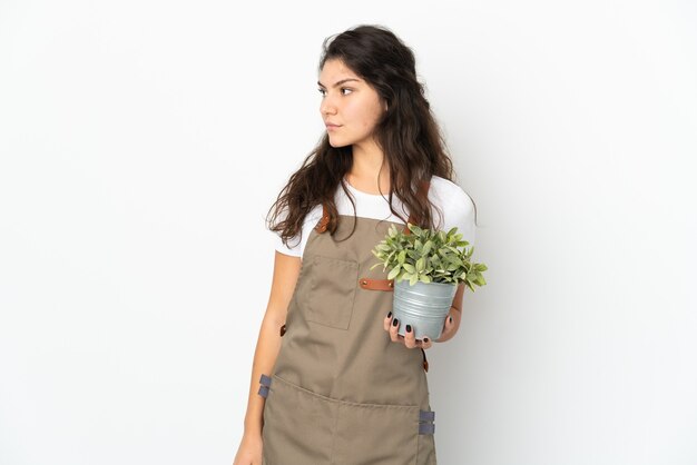 Mujer joven jardinero ruso sosteniendo una planta aislada mirando hacia el lado