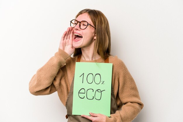 Mujer joven jardinero sosteniendo un cartel 100% ecológico aislado en fondo blanco gritando y sosteniendo la palma cerca de la boca abierta.