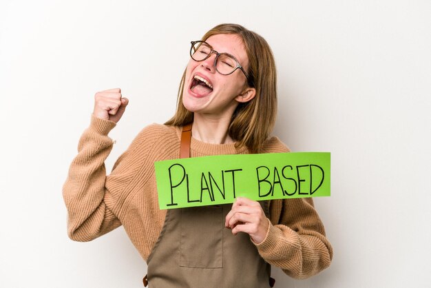 Mujer joven jardinero sosteniendo un cartel basado en un plan aislado sobre fondo blanco levantando el puño después de un concepto de ganador de la victoria