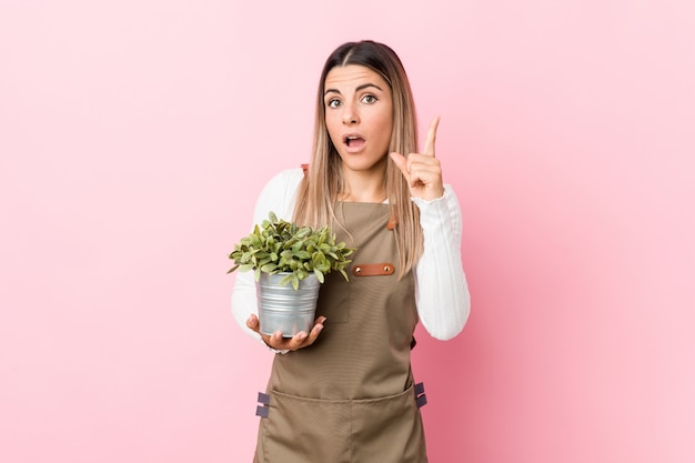 Mujer joven jardinero sosteniendo una planta teniendo una idea