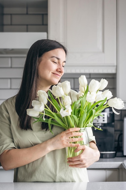 Mujer joven y jarrón con un ramo de tulipanes blancos en la cocina