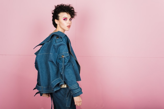 Mujer joven en jeans estilo posando en pared rosa