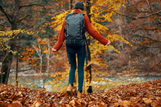 Mujer joven en jeans y un suéter con una mochila en la espalda camina en el parque en otoño en la vista inferior de la naturaleza