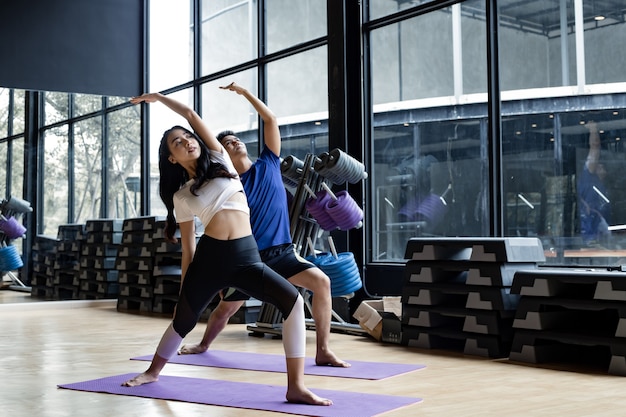 Mujer joven y joven de pie yoga en la estera de yoga en la sala de ejercicios con espacio de copia. Parejas jóvenes con ejercicio haciendo yoga juntos en interiores. Concepto de ejercicio con yoga.