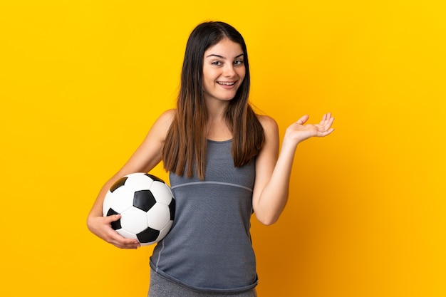 Mujer joven jugador de fútbol aislada en amarillo con expresión facial sorprendida