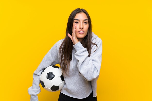 Mujer joven del jugador de fútbol aislada en amarillo que susurra algo