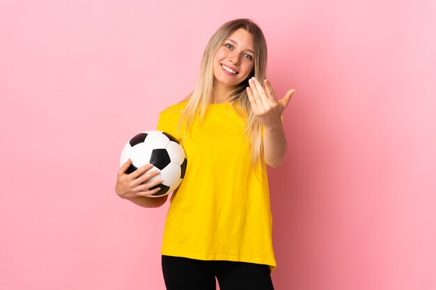 Mujer joven jugador de fútbol aislada en rosa invitando a venir