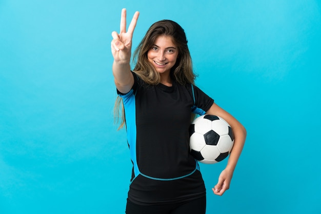 Mujer joven jugador de fútbol aislado en azul sonriendo y mostrando el signo de la victoria