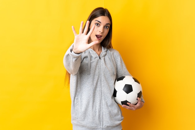 Mujer joven jugador de fútbol aislado en la pared amarilla contando cinco con los dedos